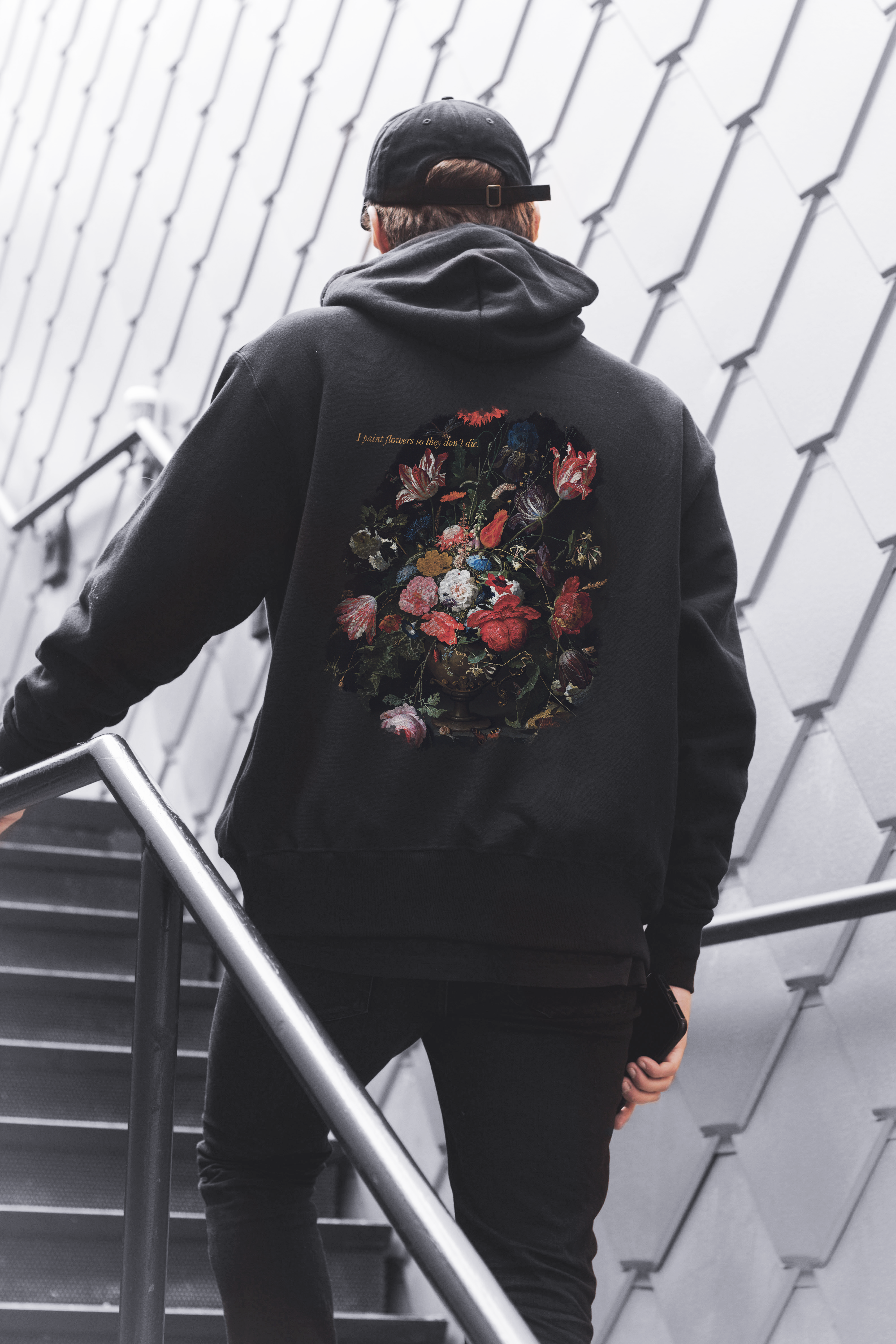Person wearing a black hoodie with floral design on the back, standing on a staircase.
